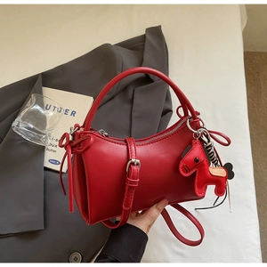 Detail of red leather crossbody bag with wooden horse charm and elegant bow on gray background