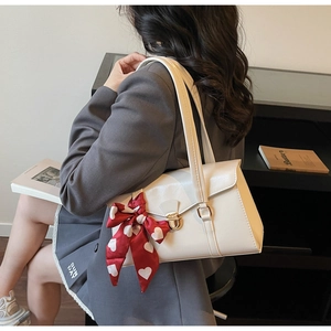 Détail du sac sous l'aisselle en cuir blanc avec serrure dorée et nœud en ruban rouge