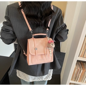 Pink patent leather backpack featuring a plush monkey charm with red plaid bow
