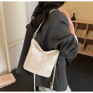 Dettaglio di una borsa a secchiello color crema con etichetta in pelle e trama tessile