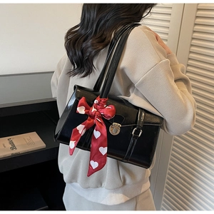 Détail d'un sac à bandoulière noir brillant avec un nœud en ruban de soie rouge