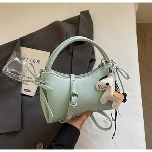 Detail of mint green crossbody bag with cartoon pony charm on grey blazer backdrop