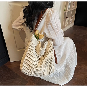 Detail of a woven hollow-out tote bag with brown leather straps and a floral accent