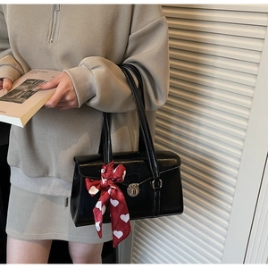 Détail d'un sac à main en cuir verni noir avec fermoir argenté et foulard cœur rouge