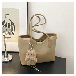 Dettaglio della borsa tote in tela kaki con pelle, logo e un ciondolo a forma di cane di peluche