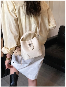 Detail view of white bucket bag with metal twist lock, handle, and brown bear pendant