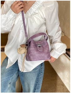 Detailed close-up of purple suede bucket bag with silver clasp and plush bear charm