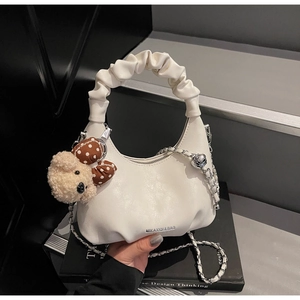 Detail of white pleated cloud bag featuring silver chain strap and cute teddy bear charm