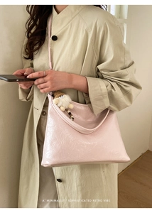 Borsa sottobraccio in pelle plissettata rosa con ciondolo in peluche su trench beige