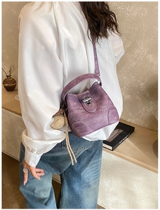 Detail view of purple leather bucket bag with metal twist lock and plush charm on model