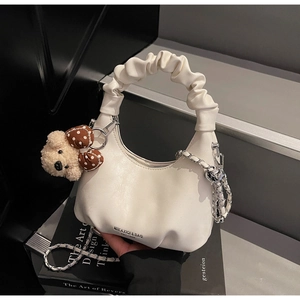 Close-up of white crescent bag with pleated handle, bear charm, and silver woven chain