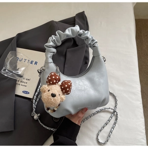 Detail of light blue hobo bag featuring a ruffled cloud handle and a teddy bear pendant