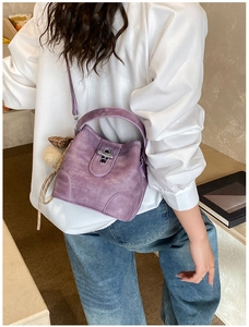 Detail of purple matte bucket bag with metal lock and plush charm on white shirt model