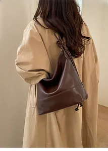 Detail of a large brown glossy PU leather tote bag with a unique knotted shoulder strap