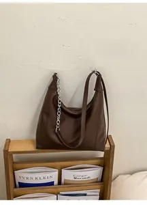 Close-up of brown leather Hobo bag with silver chain detail on a wooden magazine rack