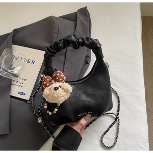 Detail of black pleated handle handbag with silver chain and cute plush bear charm