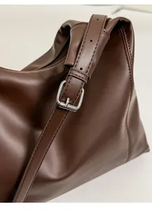 Detail of silver metal buckle and shiny brown faux leather texture on the tote bag