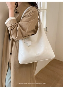 Close-up of white leather tote bag with decorative knot detail on a beige trench coat