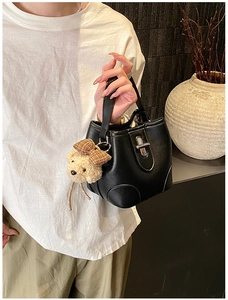 Detailed shot of black bucket bag featuring a silver metal turn-lock and cute plush bear charm