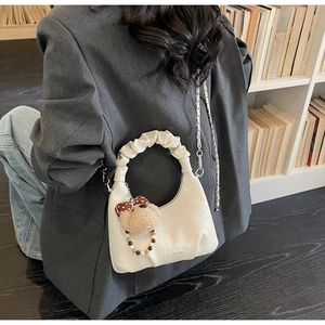 Creamy white dumpling bag with teddy bear pendant and ruched handle detail in a lifestyle setting