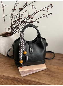 Détail d'un sac cabas en cuir noir mat avec foulard à pois et perles en bois jaunes