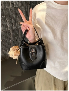 Detailed view of black leather bucket bag with silver oval lock and plush bear charm