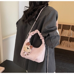 Detail of pink half-moon bag featuring pleated handle, metal chain, and cute bear charm
