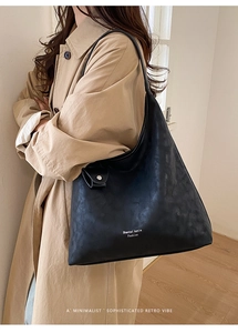 Detail view of black leather tote bag with white lettering over a beige trench coat