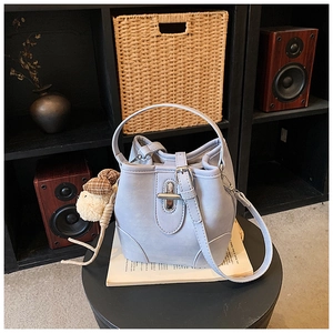 Detail of light blue bucket bag with vintage metal lock and plush bear charm on a stand