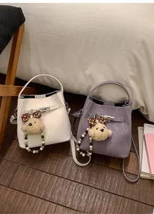 Close-up of off-white and lavender bucket bags with metallic buckles and plush bear charms