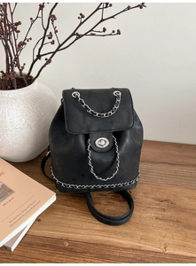 Detail of black faux leather backpack with silver chain and metal turn-lock on wood surface