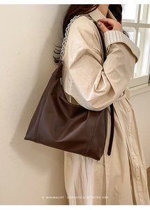 Detail of dark brown leather tote with silver chain strap on a striped shirt dress