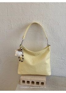 Dettaglio della borsa sottobraccio giallo chiaro con texture stropicciata e charm