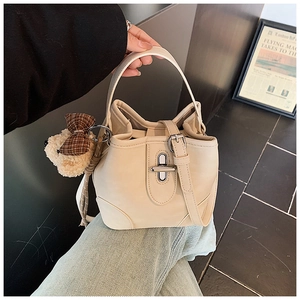 Creamy white bucket bag detail with plush bear charm and metallic twist lock closure