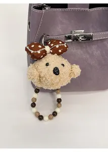 Detail of cute beige plush puppy bag charm with beaded ring on a purple leather bag