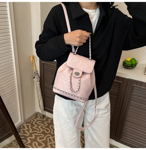 Pink faux leather backpack with silver chain details shown on model in home setting