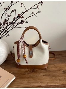 Détails d'un sac seau bicolore avec un fermoir en métal et un foulard en soie imprimé