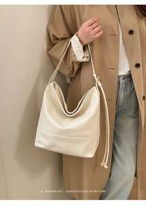 Minimalist beige tote bag shown worn over the shoulder with khaki trench coat