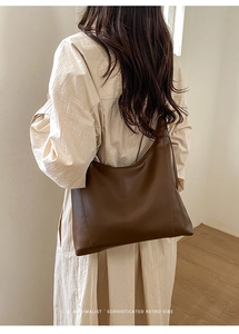 Rear view of a model carrying a large dark brown faux leather tote bag in a minimalist room