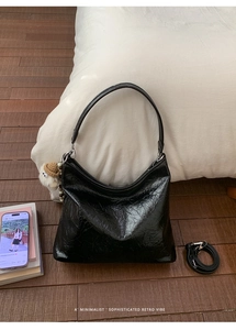 Dettaglio della borsa hobo nera lucida a pieghe con un simpatico ciondolo a bambolina