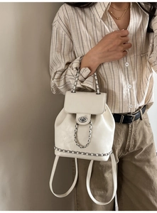 Detail view of white leather mini backpack featuring silver chain and turn-lock closure