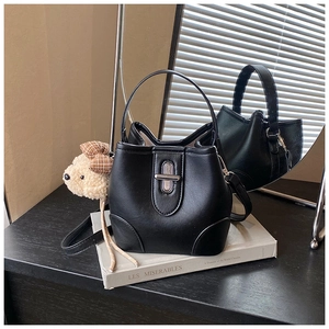Detail of black bucket bag with silver twist lock and plush bear charm on books