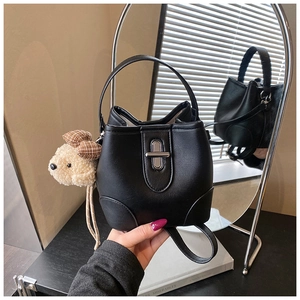 Detail of black PU leather bucket bag featuring a silver twist lock and plush puppy charm
