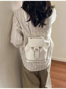 Detail of white leather backpack showing silver chain trim and metal twist lock closure