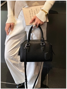 Minimalist black pebble leather Boston bag with silver hardware worn by a model in white
