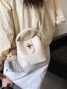 Minimalist cream bucket bag with teddy bear charm and adjustable shoulder strap