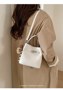 White minimalist shoulder bag with bear charm shown on a model in a trench coat