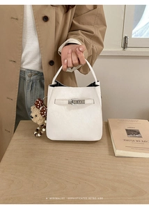 Detail of white bucket bag featuring silver turn-lock clasp and plush bear charm
