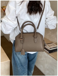 Close-up of a deep coffee leather bowling bag with twin handles and detachable strap