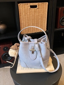 Minimalist light blue bucket handbag with plush dog charm on a vintage side table